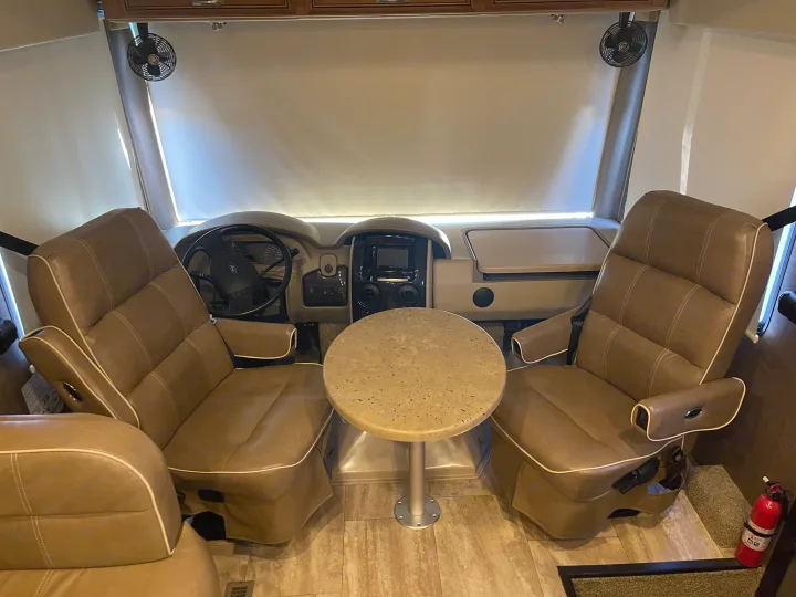 RV rental cockpit view: Tan leather captain's chairs, dashboard, central table, and ceiling fans.. Thor Challenger 2017