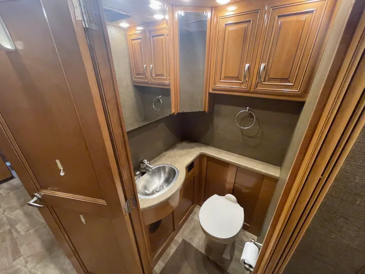 Compact RV rental bathroom with sink, toilet, mirror, and wood cabinetry. Practical and tidy.. Thor Challenger 2017