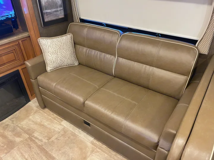 Comfortable RV rental living area featuring a plush leather sofa, TV, and electric fireplace for cozy travel.. Thor Challenger 2017