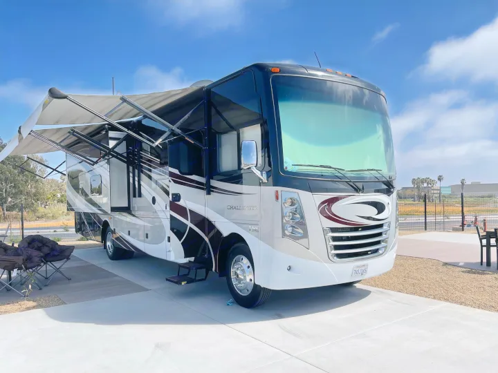 A large, modern Thor Challenger motorhome, perfect for an RV rental, is parked with its awning extended under a blue sky.. Thor Challenger 2017