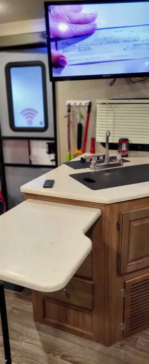 RV rental kitchen: TV shows a 'Cook-It' check for over a million dollars. Sink, pull-out counter, and remote on display.. Forest River Flagstaff Micro Lite 2018