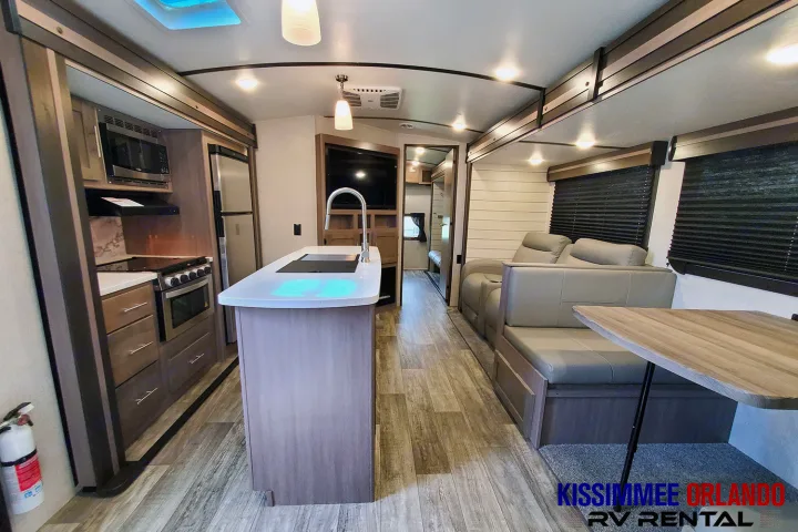 Modern RV rental interior featuring a full kitchen with island, living area with sofa, dinette, and entertainment setup.. Crossroads Sunset Trail 2022