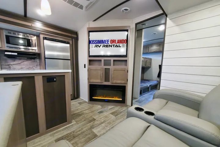 Modern RV rental interior: well-equipped kitchen, comfy recliners with cupholders, fireplace, and separate bunk room.. Crossroads Sunset Trail 2022