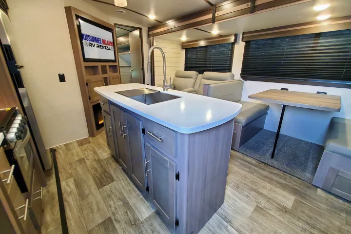 Modern RV rental interior with a central kitchen island, sink, living area with recliners, and dinette.. Crossroads Sunset Trail 2022