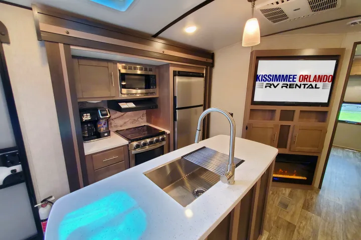 Inside a modern RV rental: well-equipped kitchen with sink, stove, fridge, plus TV & electric fireplace.. Crossroads Sunset Trail 2022