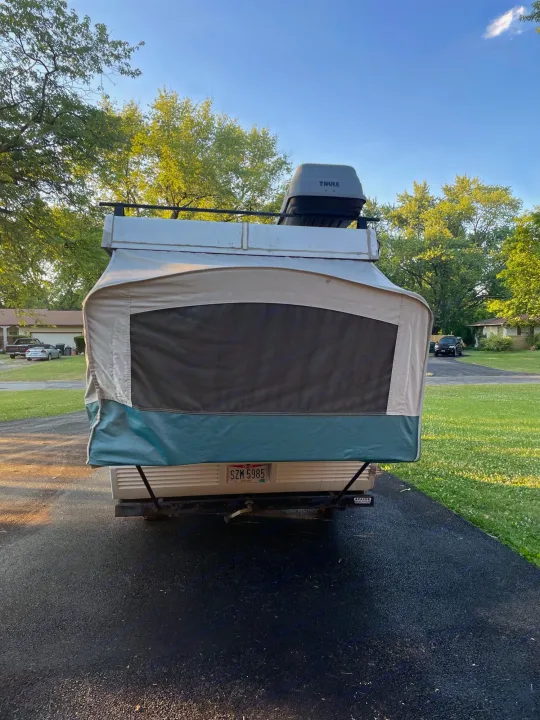 Pop-up RV rental, beige with green trim & mesh window, parked on paved driveway. Features Thule cargo box.. Coleman Destiny Taos 1996