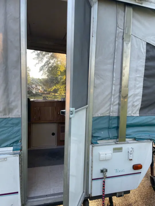 Pop-up RV rental: open door reveals a compact kitchen, light flooring, and sunny outdoor view for camping.. Coleman Destiny Taos 1996