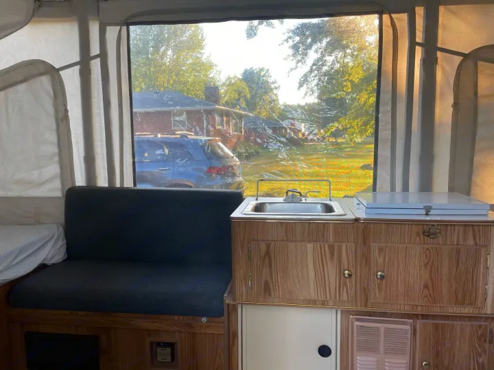 Pop-up RV rental interior with a cozy bench, sink, and a clear window view of a residential area.. Coleman Destiny Taos 1996