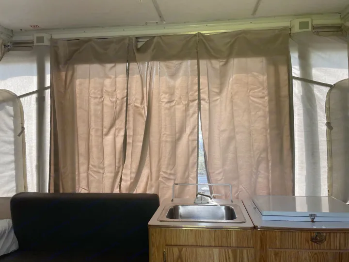 RV rental interior: small kitchen with sink, counter, and light brown privacy curtains covering pop-up camper windows.. Coleman Destiny Taos 1996