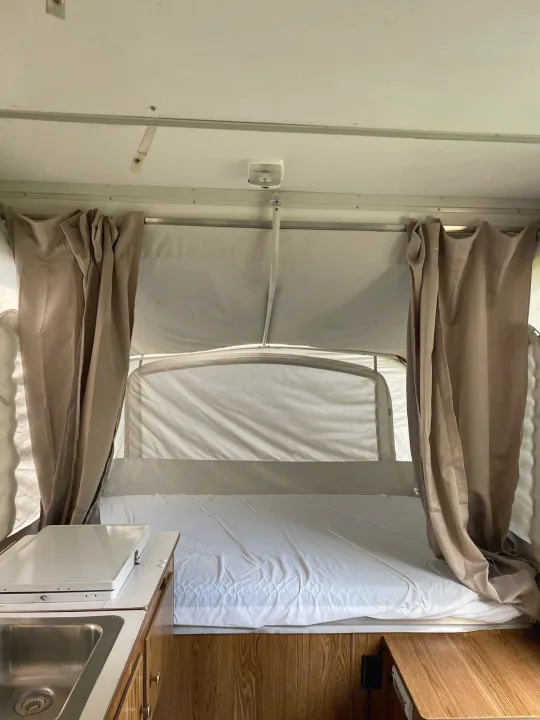 Pop-up camper RV rental interior, showing a bed, kitchen counter with sink, and curtains.. Coleman Destiny Taos 1996