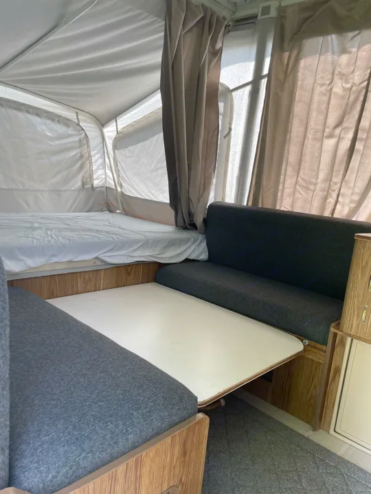 Inside an RV rental, featuring a pop-up bed, dinette with table & upholstered benches, and curtains.. Coleman Destiny Taos 1996