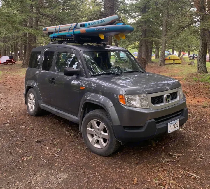 Grey Honda Element with paddleboards, parked at a wooded campground. A great alternative to an RV rental.. Honda Element 2009