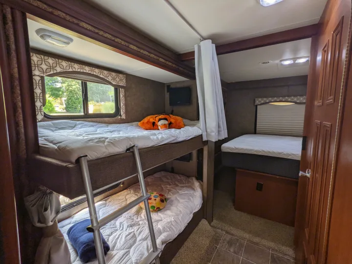 Step inside this RV rental: a compact bedroom with comfortable bunk beds, a main bed, and natural light from a window.. Thor Four Winds 2013