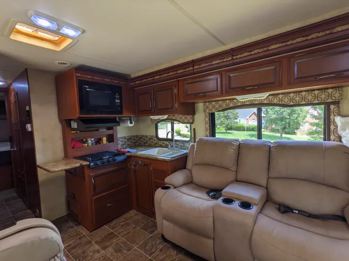 Modern RV rental interior: full kitchen, comfy recliners with cup holders, and ample natural light from windows.. Thor Four Winds 2013