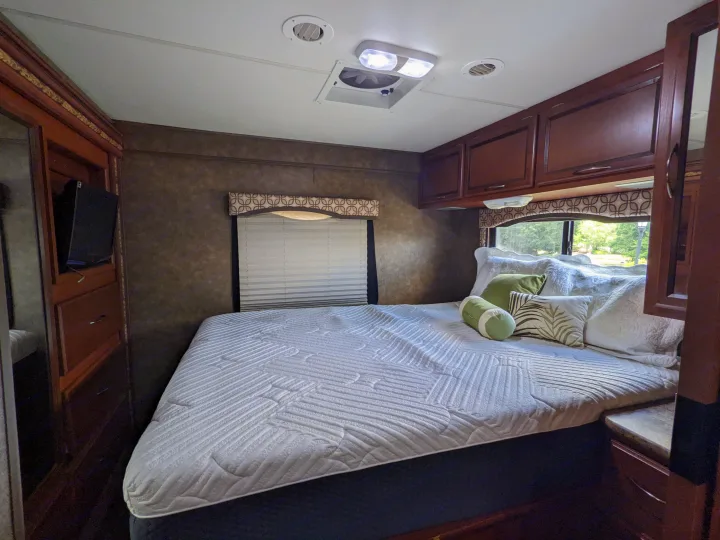 Experience this RV rental's cozy bedroom, featuring a comfortable bed with white quilting, wooden cabinets, and a window.. Thor Four Winds 2013