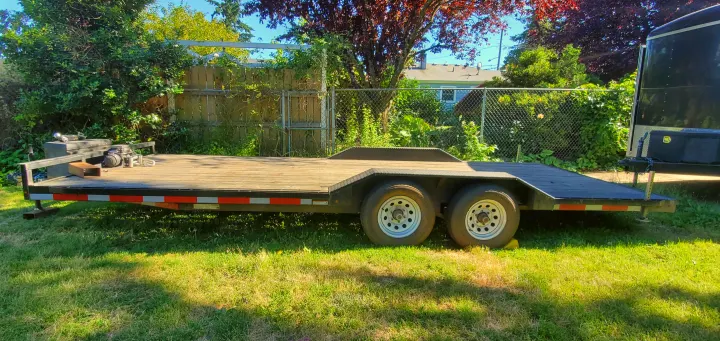 A black flatbed utility trailer with wooden deck and four wheels on grass. Ideal for hauling gear related to RV rental trips.. Eagle flatbed 2019
