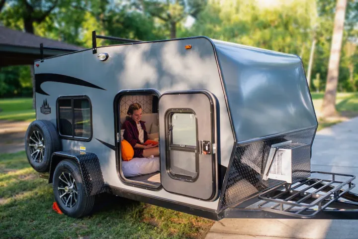 Cozy rv rental: A young woman sits comfortably reading inside a gray teardrop camper with the door open, set outdoors.. Superior Lite Camper Deluxe 2022