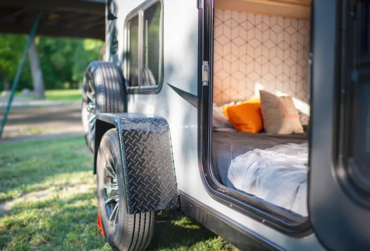 Close-up of a compact RV rental camper parked on grass, door open revealing a comfortable bed & modern patterned interior.. Superior Lite Camper Deluxe 2022