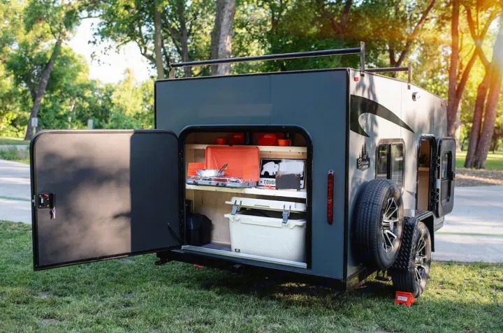 Discover this compact RV rental with an open rear hatch revealing a fully equipped outdoor kitchen, ideal for camping adventures.. Superior Lite Camper Deluxe 2022