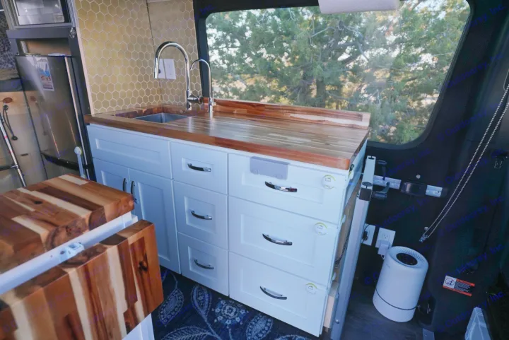 Custom RV rental kitchen featuring white cabinets, wood counters, hexagonal backsplash, and child-proof drawer latches.. Mercedes-Benz Sprinter 2021