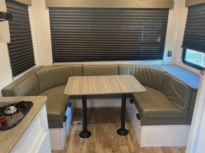 Spacious RV rental dinette featuring U-shaped bench seating, a light-colored table, and dark pleated window blinds.. Keystone RV Hideout 2022