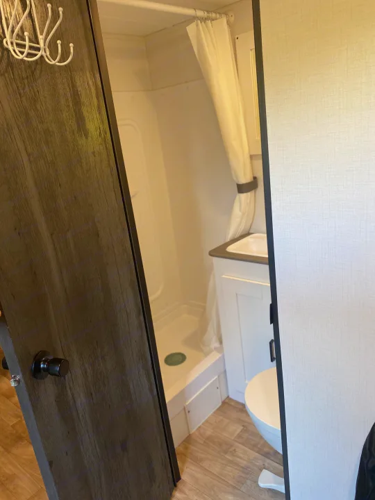 Inside a compact RV rental, this bathroom features a shower, sink, toilet, and door with hooks.. Keystone RV Hideout 2022