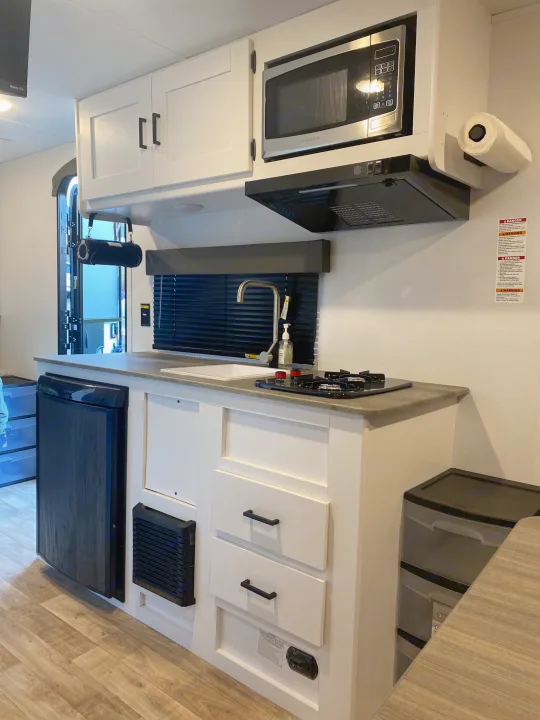 Inside this RV rental, a modern kitchen: white cabinets, microwave, sink, two-burner stove, and fridge. Essential for travel.. Keystone RV Hideout 2022