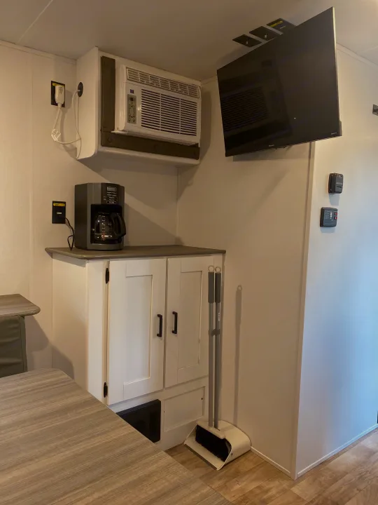 An RV rental's kitchen and dining area, complete with an AC unit, TV, coffee maker, and broom.. Keystone RV Hideout 2022