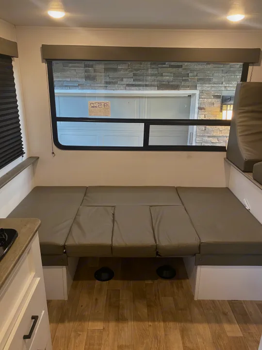 RV rental interior showcasing a spacious, gray dinette that converts to a bed. Window view outside. Ready for adventure!. Keystone RV Hideout 2022