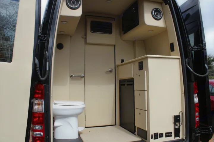 RV rental: Compact camper van interior with toilet, middle door, and right-side kitchenette featuring a fridge and storage.. Ultimate Toys Ultimate Coach 2023