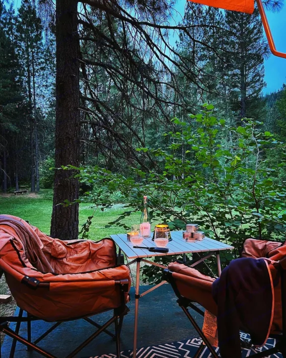RV rental: Peaceful camping setup with two chairs and a table holding rosé and glasses, surrounded by lush forest.. Airstream Bambi 2022