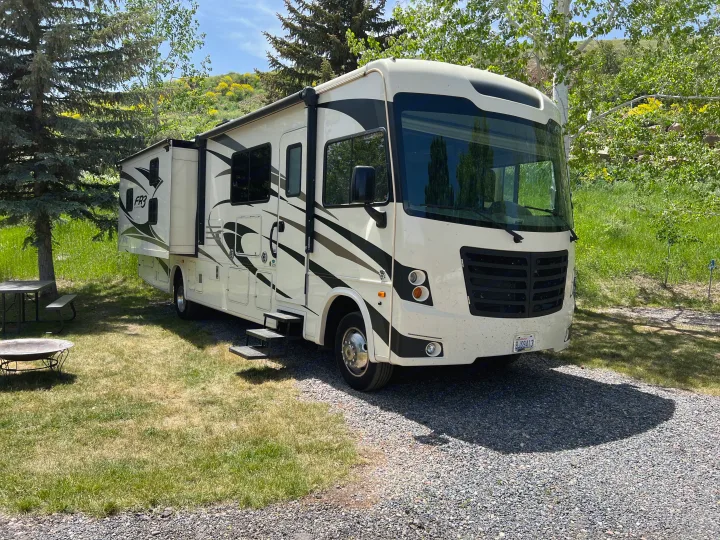 Spacious white and black RV rental parked on gravel at a sunny campsite with extended slide-out, picnic table, and fire pit.. Other Other 2018
