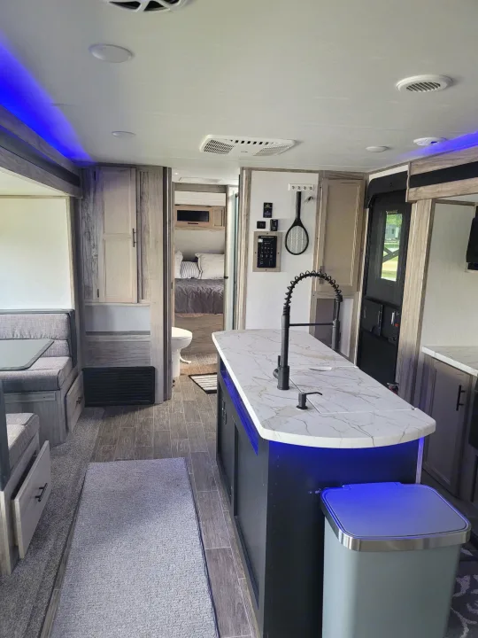 Stylish RV rental interior: kitchen island with blue light, cozy dinette, and bedroom view.. Forest River Cherokee Alpha Wolf 2021