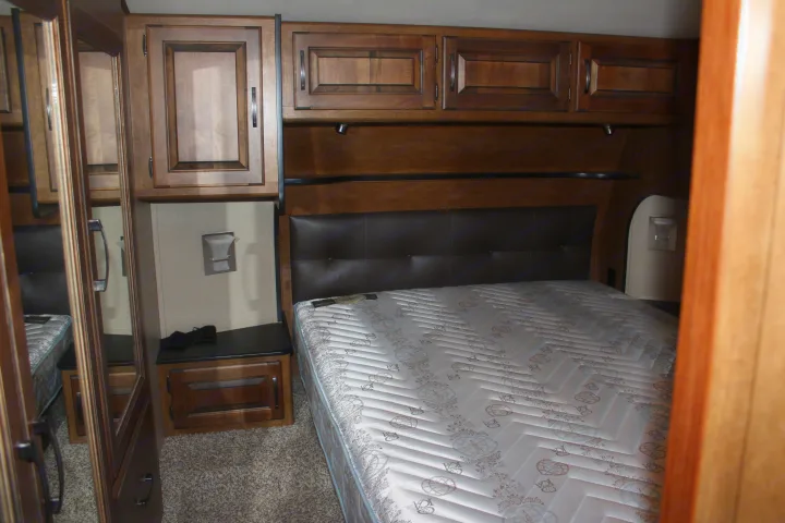 RV rental bedroom featuring a bed, padded headboard, and overhead wood cabinets. Compact and functional.. Grand Design Reflection 2015