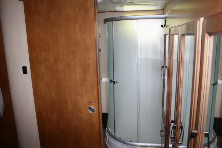 This RV rental offers a compact bathroom with a wooden sliding door, corner frosted glass shower, and toilet area.. Grand Design Reflection 2015