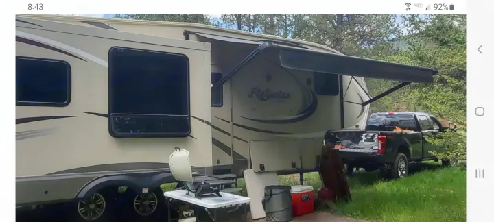 RV rental camping setup: Fifth wheel with extended awning, truck, grill, and coolers for an outdoor retreat.. Grand Design Reflection 2015