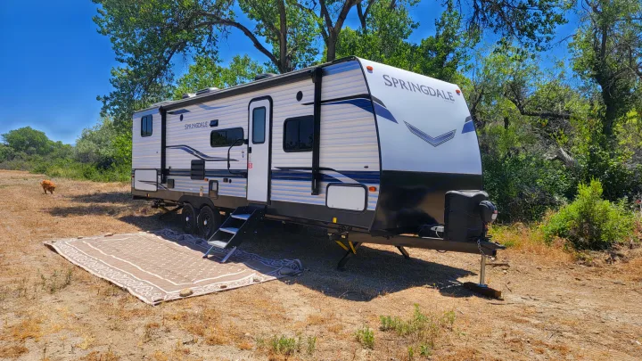 A white and blue Springdale RV rental is set up at a sunny campsite with a golden dog nearby.. Keystone RV Springdale 2022