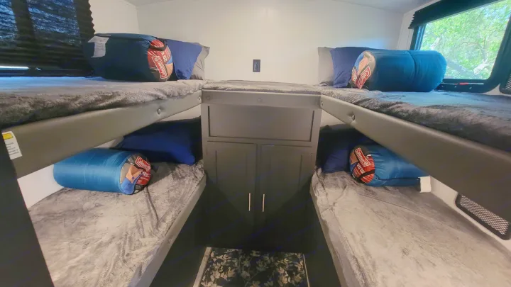 Cozy RV rental sleeping area featuring four bunk beds, each with a pillow and Coleman sleeping bag. Ideal for groups.. Keystone RV Springdale 2022