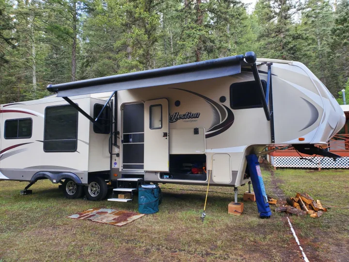Grand Design Reflection rv rental parked at a peaceful campsite with extended awning, surrounded by tall trees.. Grand Design Reflection 2015