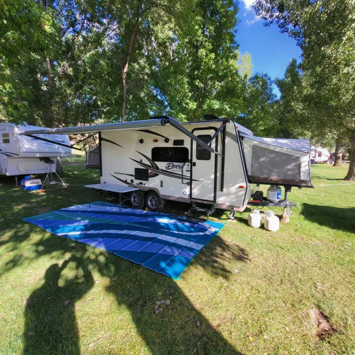 RV rental: Relaxing campsite with a hybrid travel trailer & other RVs, featuring an outdoor mat under shady trees.. Forest River Rockwood Roo 2017
