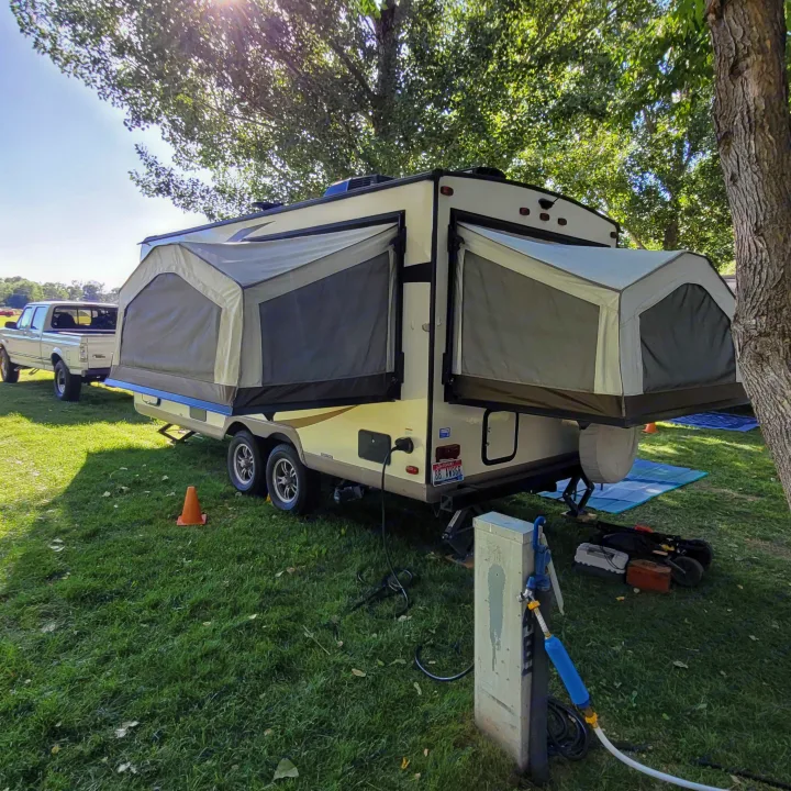 An RV rental, a pop-up hybrid trailer, is fully set up at a grassy campsite with power and water hookups under sunny skies.. Forest River Rockwood Roo 2017