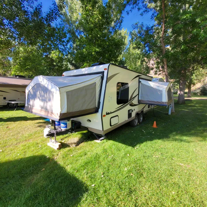 An RV rental hybrid travel trailer with its pop-out tents extended, parked on green grass in a treed campground.. Forest River Rockwood Roo 2017