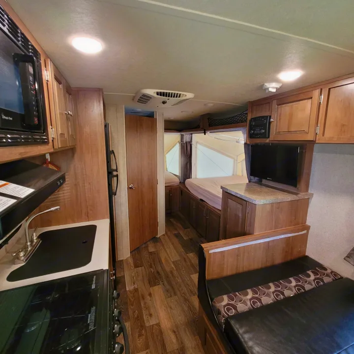 Compact RV rental interior with kitchen (microwave, stove), convertible dinette, and rear sleeping area. Perfect for trips.. Forest River Rockwood Roo 2017