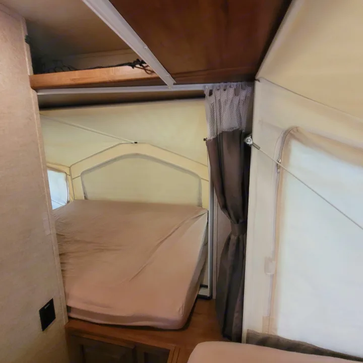 Cozy RV rental: Inside a pop-up camper, featuring a bed, fabric walls, and curtains. Perfect for camping adventures.. Forest River Rockwood Roo 2017