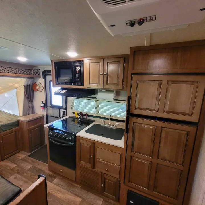 RV rental interior: Compact kitchen with stove, microwave, sink, fridge, and a pop-out sleeping area.. Forest River Rockwood Roo 2017