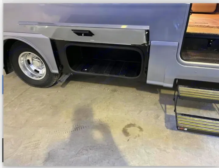 RV rental's grey exterior: open storage bay, wheel, exhaust, and retractable entry steps on concrete ground.. Winnebago View 2023
