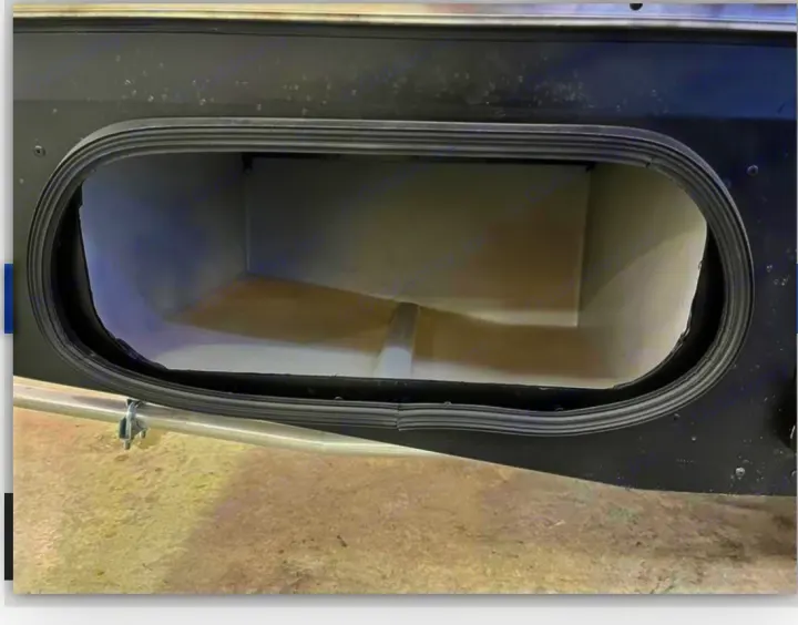 Open oval exterior storage compartment of an RV rental. Its empty, light-colored interior is visible with a black rubber seal around the dark exterior.. Winnebago View 2023