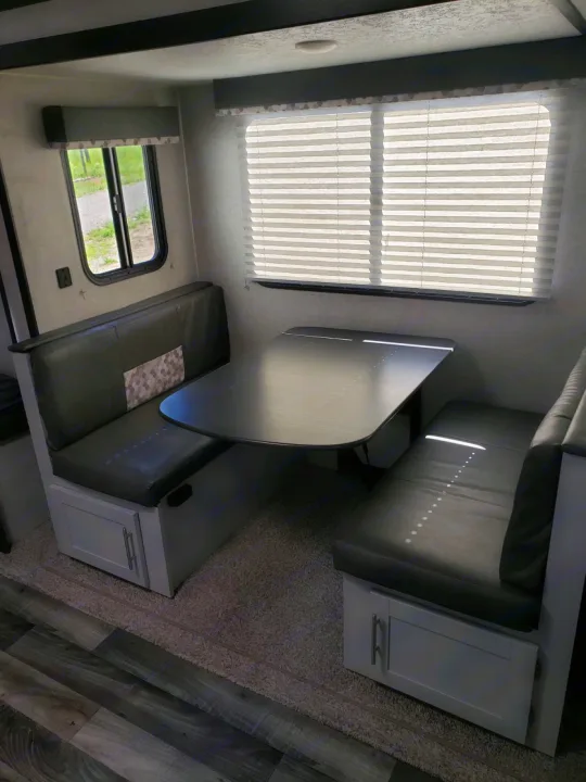 Modern RV rental dinette featuring dark upholstered booth benches, a sleek table, and under-seat storage. Bright window light.. Keystone Bullet 2020