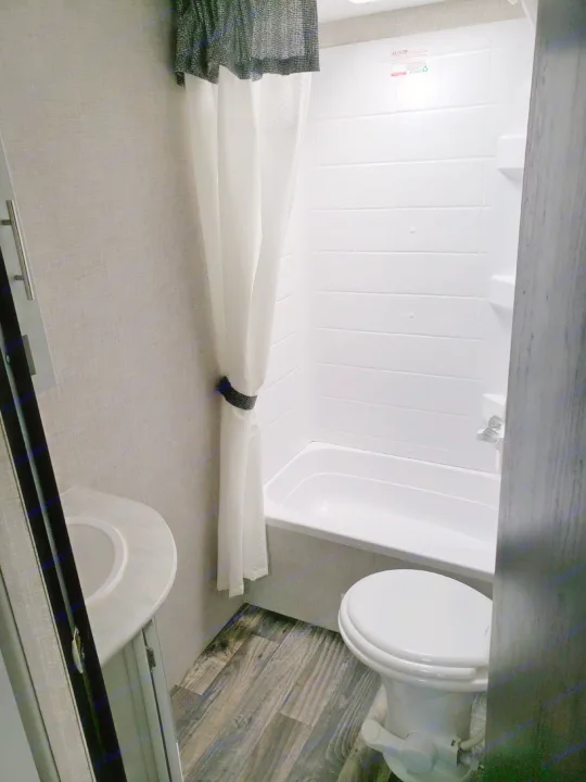 Compact RV rental bathroom with shower-tub, toilet, and corner sink. Ideal for travel convenience.. Keystone Bullet 2020