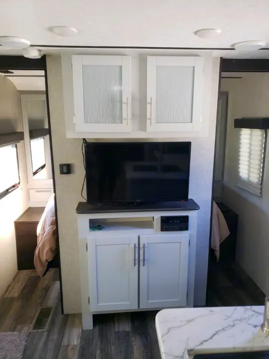 Modern RV rental interior featuring an entertainment center with TV, white cabinets, and wood-look flooring.. Keystone Bullet 2020